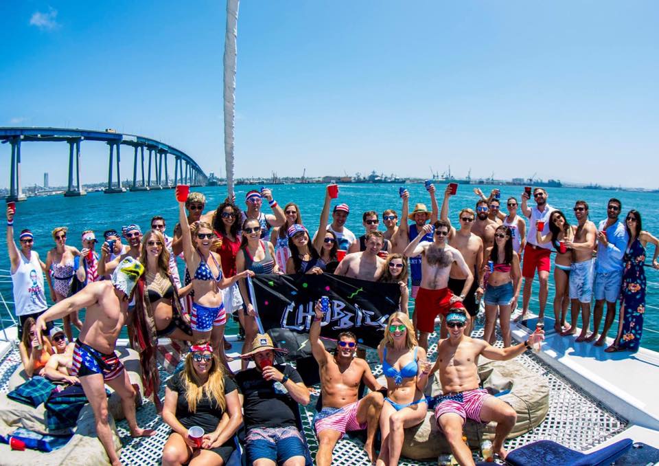 people smiling at camera, with drinks in the air, they are enjoying a day cruise on a catamaran sailboat in san diego